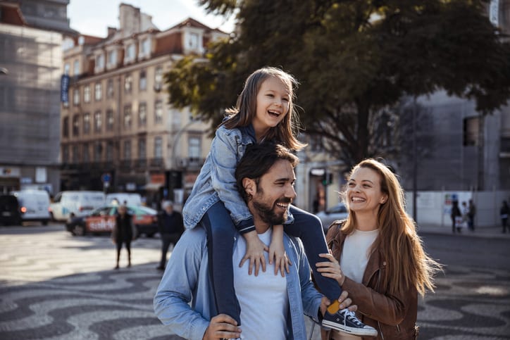 Familie på tre stykker hvor barn sitter på skuldrene til far.